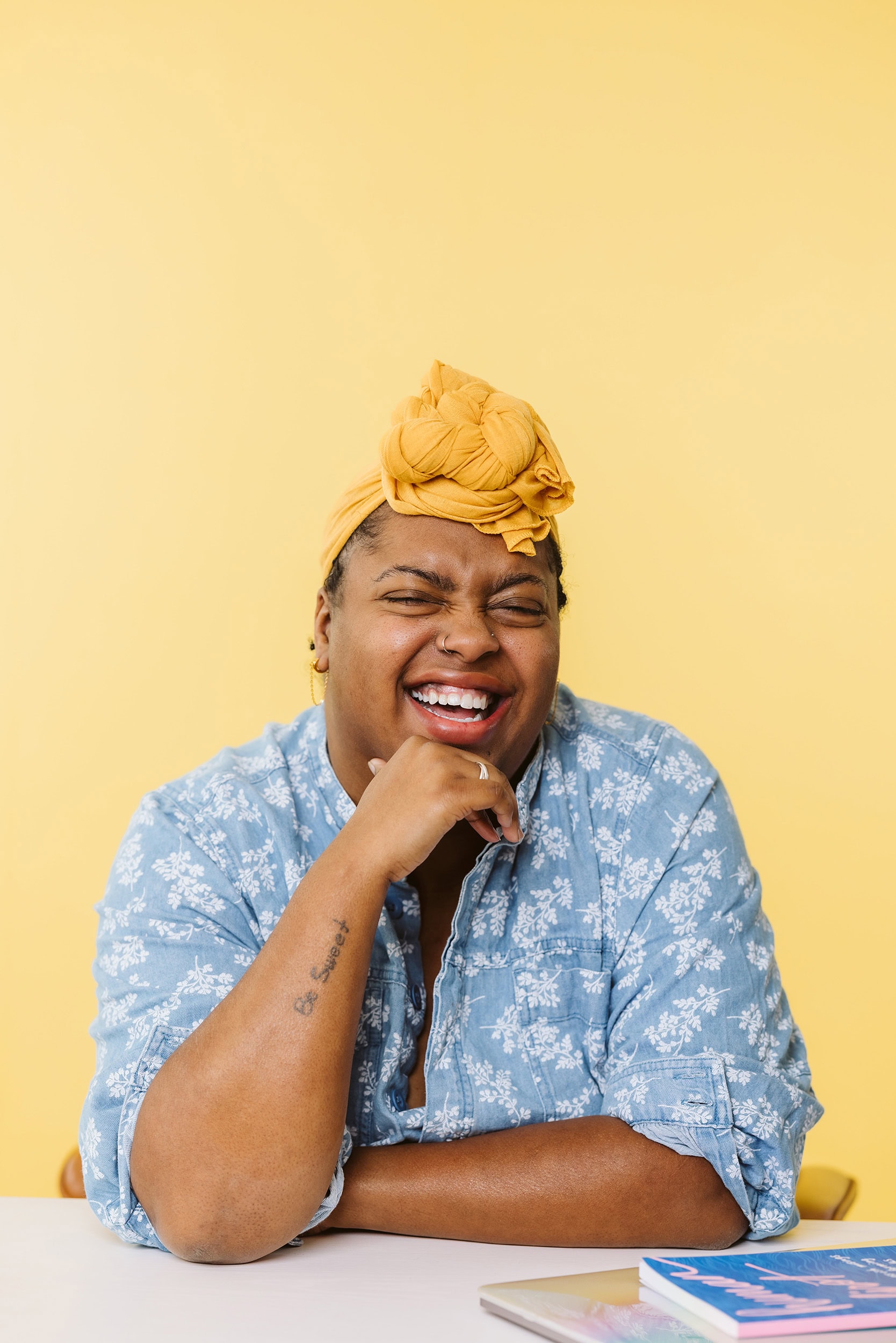 Smiling woman with vibrant yellow headwrap posing for a joyful, colorful photo.